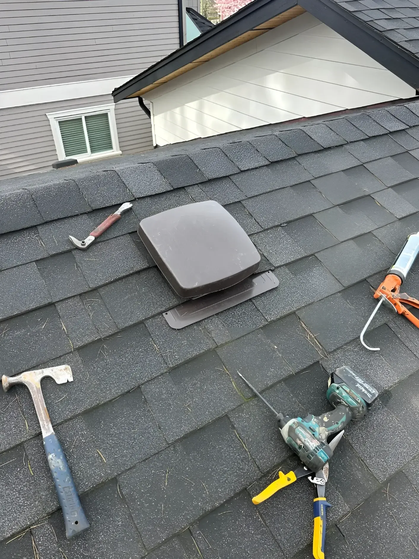 Gray roof vent on asphalt shingle roof with tools